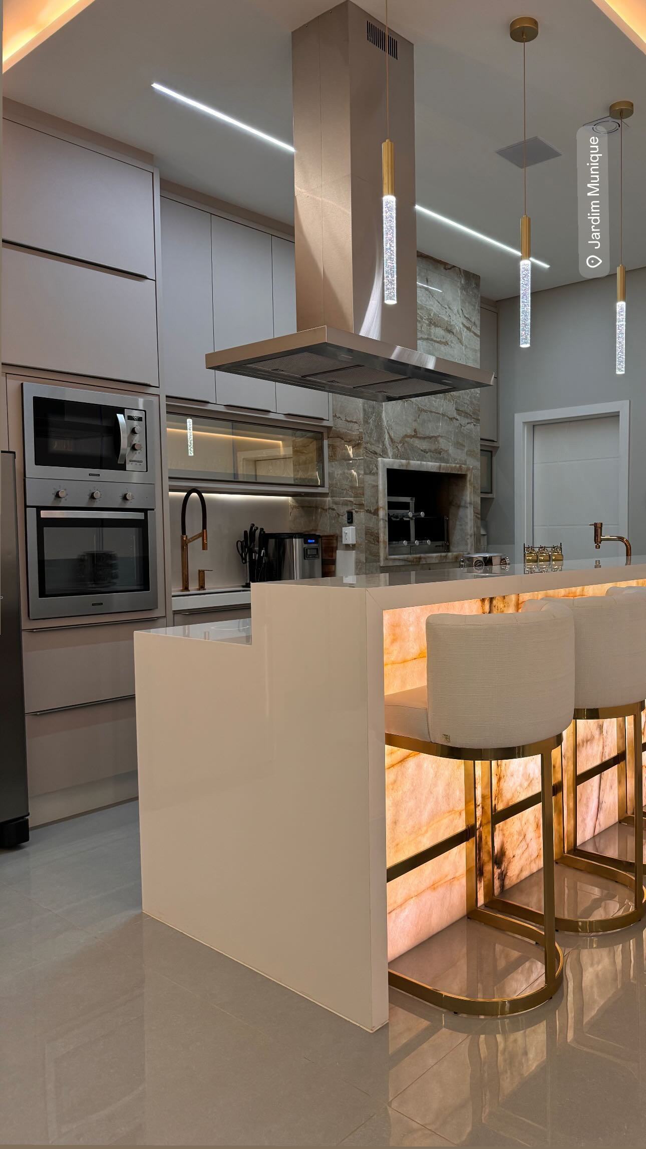 Cozinha planejada com ilha em ônix retroiluminada e acabamento dourado